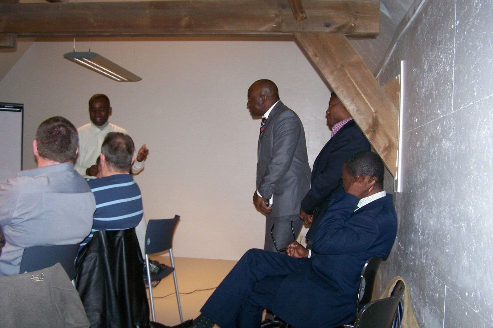 Dans une salle sous les combles, un homme debout s’adresse à des participants, assis ou debout.